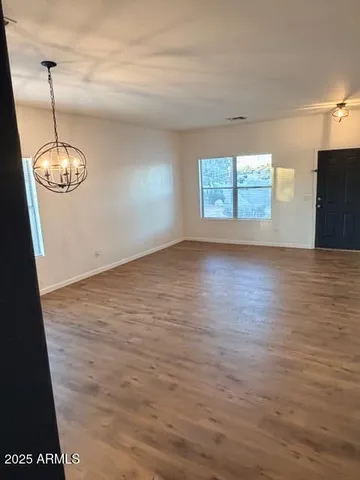 an empty room with wooden floor chandelier fan and windows