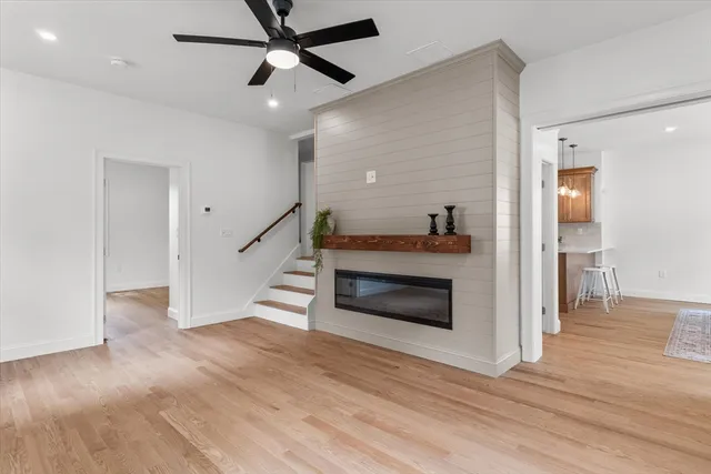 a view of a livingroom with wooden floor a ceiling fan and a kitchen space