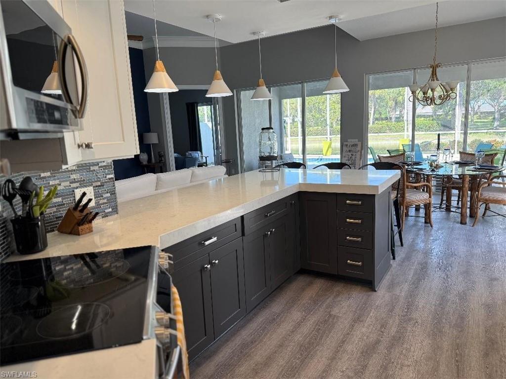 Kitchen featuring stainless steel appliances, decorative light fixtures, dark wood-style floors, a peninsula, and healthy amount of natural light