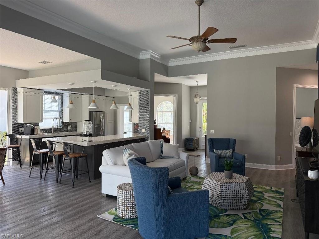 7549 Garibaldi Court Naples, FL 34114 - Photo 2 of 15 Living room featuring a textured ceiling, ornamental molding, healthy amount of natural light, ceiling fan, and dark wood-style flooring