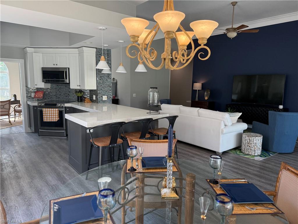 7549 Garibaldi Court Naples, FL 34114 - Photo 3 of 15 Kitchen with decorative light fixtures, stainless steel appliances, a breakfast bar, a peninsula, and white cabinetry