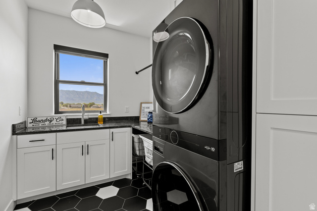 3111 South 1250 West Logan, UT 84321 - Photo 14 of 51 Laundry area featuring a stackable washer and dryer, black hexagon tile flooring, white shaker cabinetry, dark countertops, and a window overlooking a mountain landscape