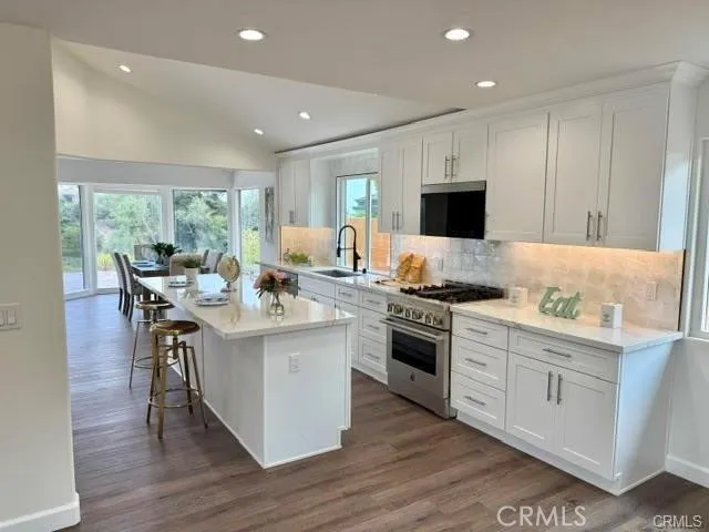 a open kitchen with stainless steel appliances granite countertop a stove top oven a sink dishwasher a dining table and chairs with wooden floor