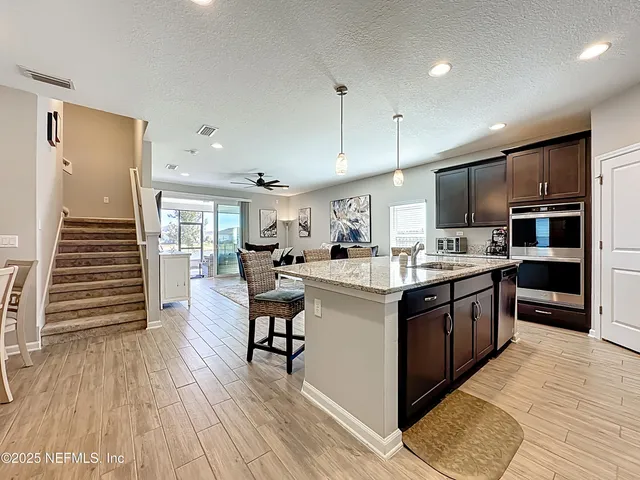 a kitchen with stainless steel appliances granite countertop a stove top oven a refrigerator a kitchen island a dining table and chairs with wooden floor