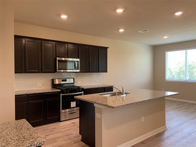 a kitchen with stainless steel appliances granite countertop a sink a stove a microwave and island with wooden cabinet