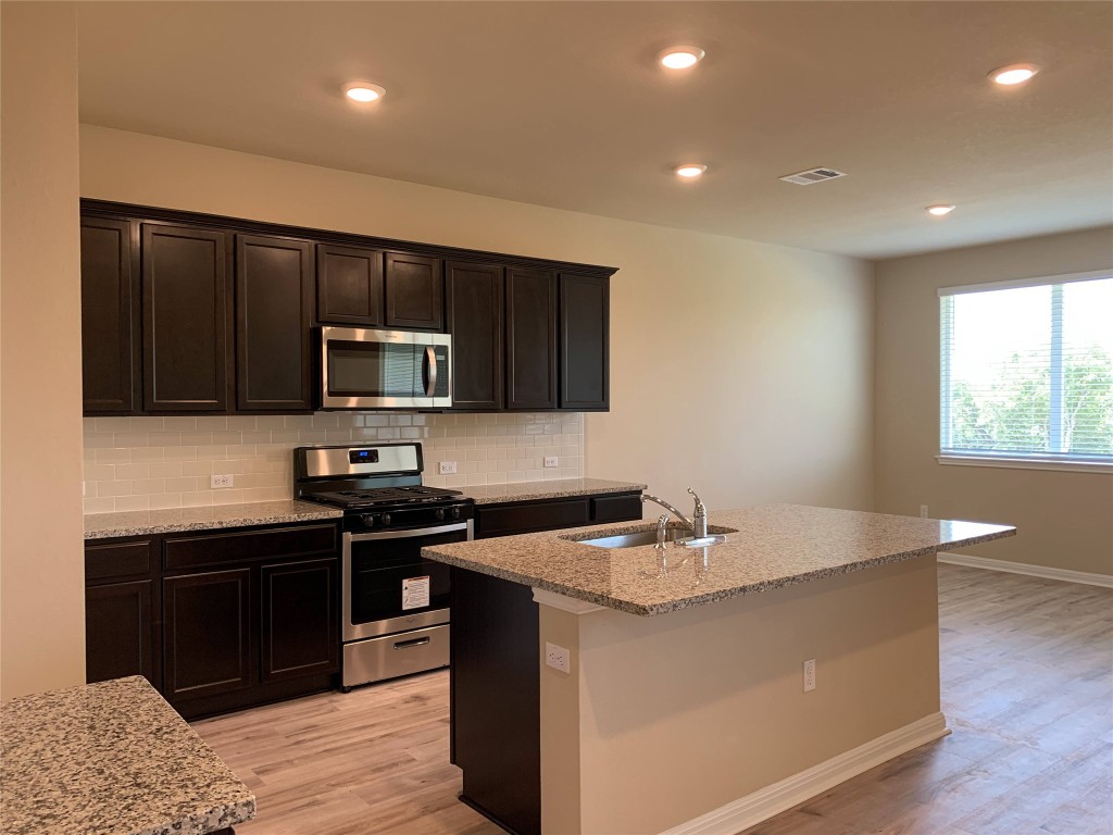 100 Royal Palm Way Leander, TX 78641 - Photo 7 of 29 a kitchen with stainless steel appliances granite countertop a sink a stove a microwave and island with wooden cabinet
