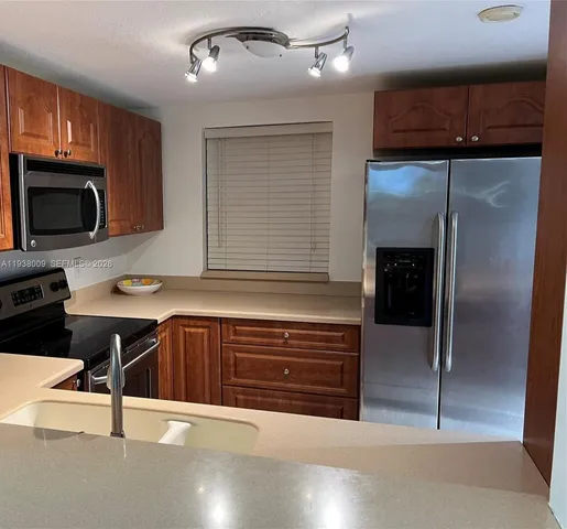 a kitchen with stainless steel appliances kitchen island granite countertop a refrigerator a stove and a sink with wooden floor