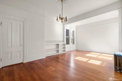 a view of an empty room with wooden floor fridge and a window