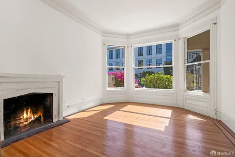 a view of an empty room with wooden floor fireplace and a window