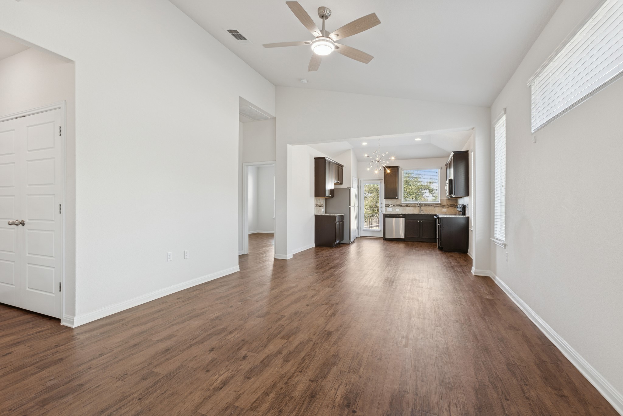 6104 Steep Cactus Trail Austin, TX 78735 - Photo 2 of 17 The property features a spacious open-concept living area with wood-look flooring and white walls, leading into a kitchen with dark cabinetry, stainless steel appliances, and a window providing natural light