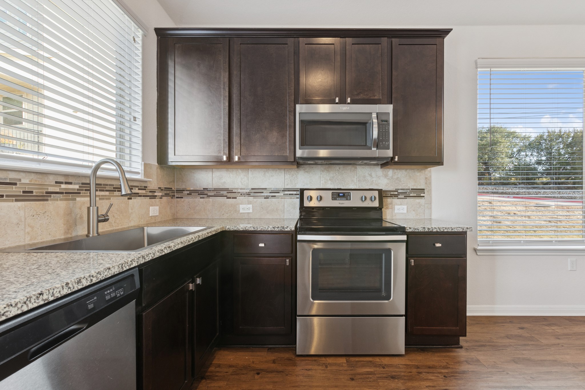 6104 Steep Cactus Trail Austin, TX 78735 - Photo 6 of 17 The kitchen features granite countertops, dark wood cabinetry, a stainless steel sink with a gooseneck faucet, and stainless steel appliances including a microwave, range, and dishwasher
