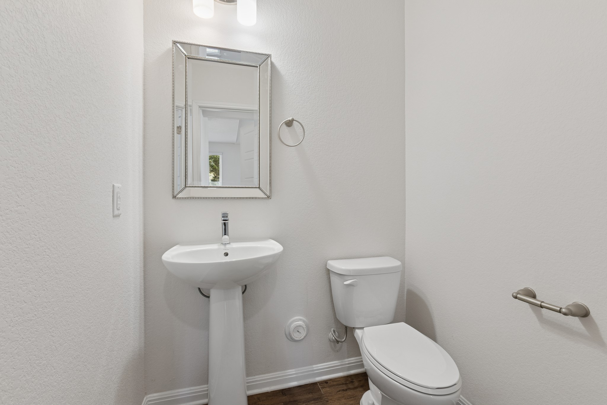 6104 Steep Cactus Trail Austin, TX 78735 - Photo 7 of 17 The property features a bathroom with a white pedestal sink, a toilet, a decorative mirror, and a wall-mounted light fixture