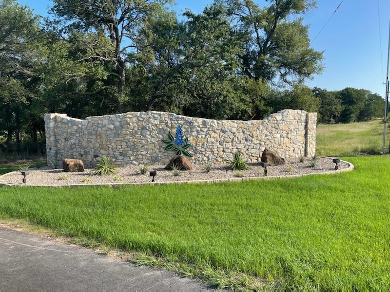 Community sign with a lawn and view of wooded area