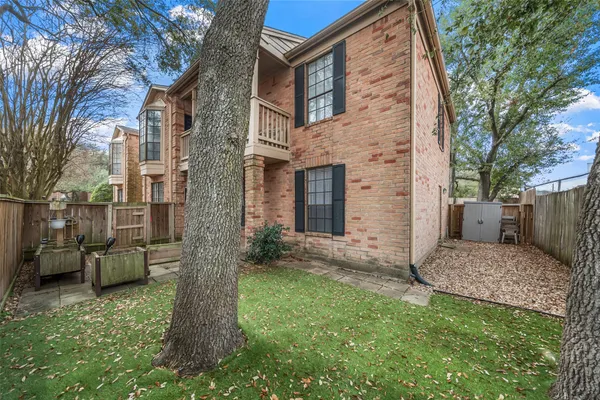 a view of a brick house with a small yard and large tree