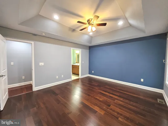 a view of an empty room with wooden floor and a ceiling fan