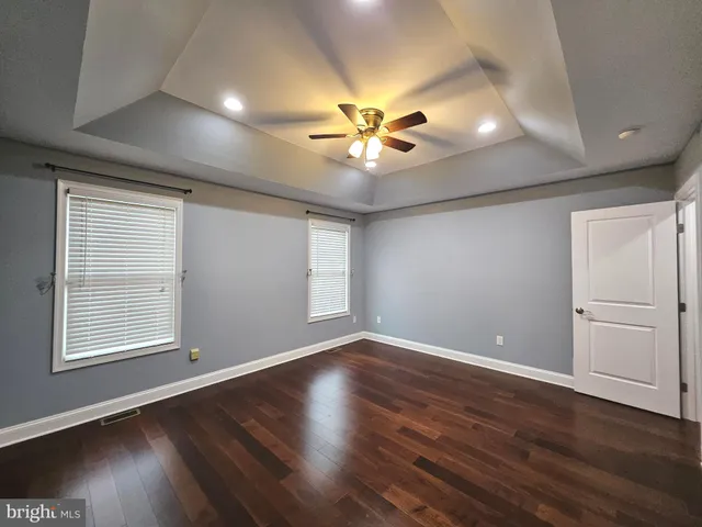 an empty room with wooden floor chandelier fan and windows