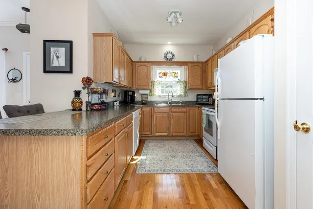 a kitchen with granite countertop a refrigerator a sink dishwasher a stove and white countertops with wooden floor