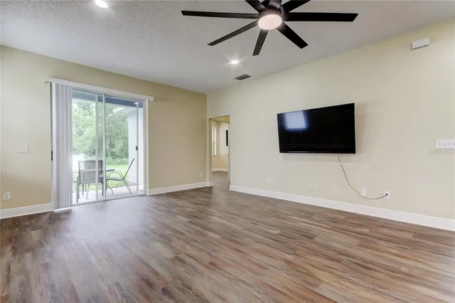 a view of an empty room with wooden floor and fan