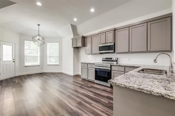 a kitchen with granite countertop a stove top oven a sink dishwasher and a refrigerator with wooden floor