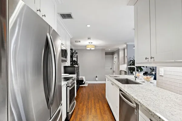 a kitchen with stainless steel appliances granite countertop a refrigerator a sink and white cabinets