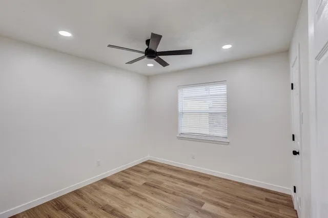 an empty room with wooden floor ceiling fan and windows