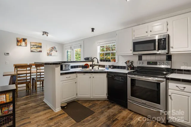 a kitchen with stainless steel appliances granite countertop a stove top oven a sink dishwasher and white cabinets with wooden floor