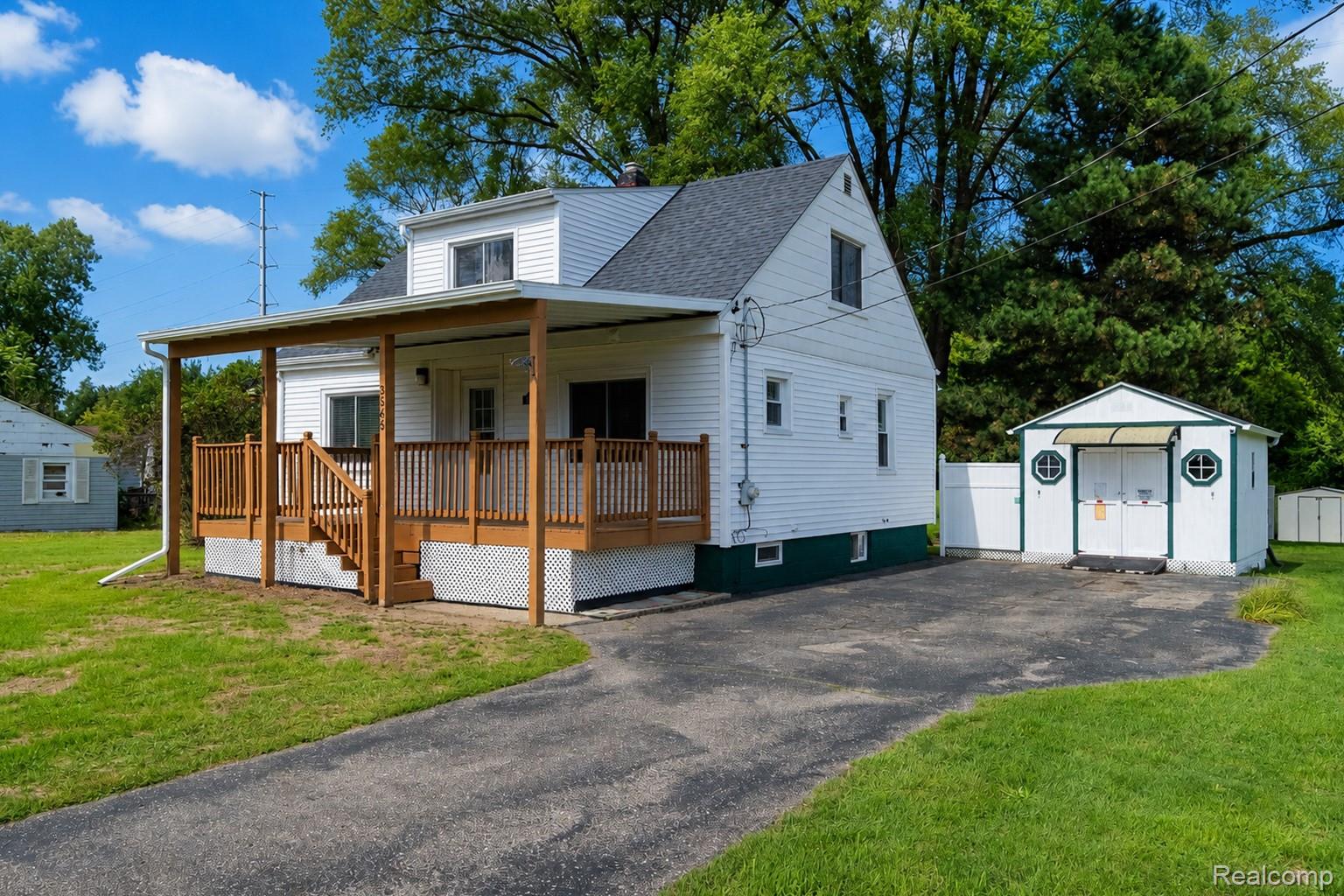 3363 East Pierson Road Flint, MI 48506 - Photo 2 of 27 White siding residence featuring a covered wooden deck, paved driveway, and detached storage shed