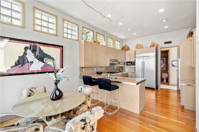 a kitchen with stainless steel appliances kitchen island granite countertop a refrigerator a stove a dining table and chairs with wooden floor