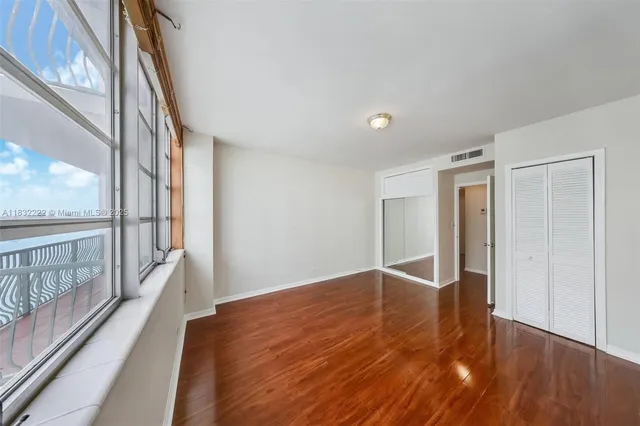 a view of an empty room with wooden floor and a window
