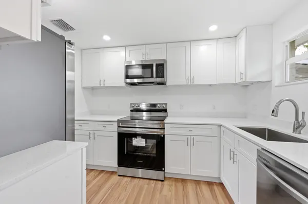 a kitchen with stainless steel appliances granite countertop a sink dishwasher a refrigerator and white cabinets with wooden floor