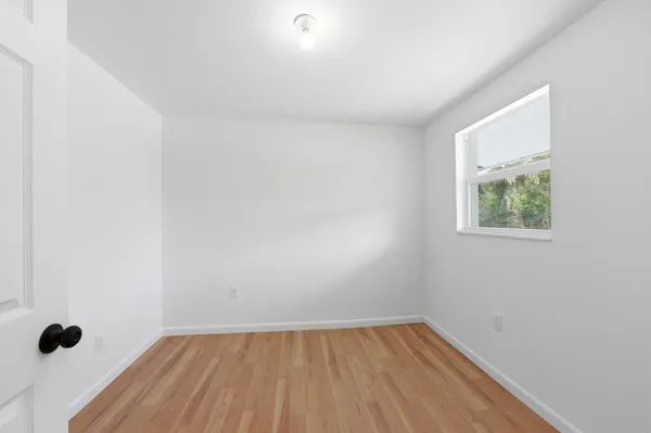 a view of an empty room with wooden floor and a window