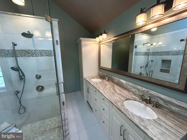 a bathroom with a granite countertop double vanity sink mirror and shower