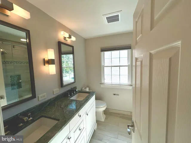a spacious bathroom with a granite countertop sink a toilet a mirror and window