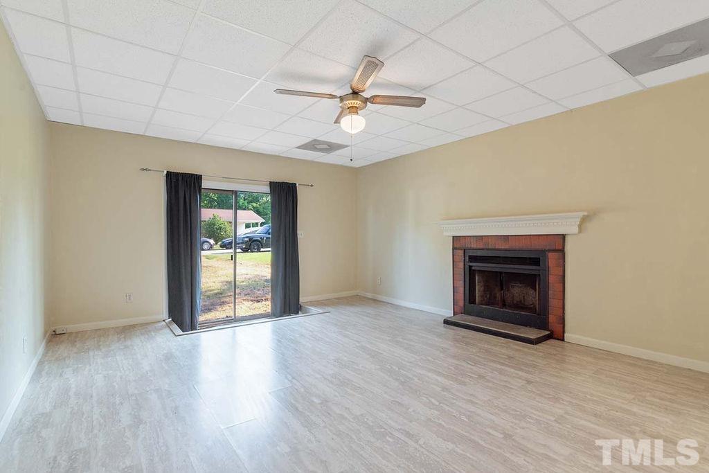 3806 Lee Road Raleigh, NC 27604 - Photo 5 of 33 an empty room with wooden floor a ceiling fan a fireplace and windows