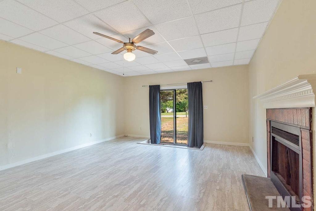 3806 Lee Road Raleigh, NC 27604 - Photo 6 of 33 an empty room with wooden floor a ceiling fan and fireplace
