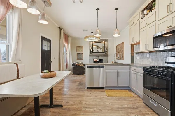 a kitchen with stainless steel appliances kitchen island granite countertop a stove a sink dishwasher and white cabinets with wooden floor