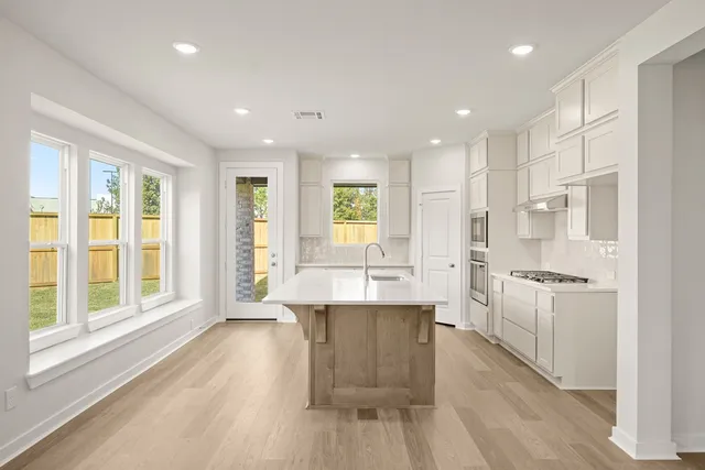 a large kitchen with kitchen island a large window a sink stainless steel appliances and cabinets