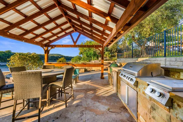 a view of a patio with table and chairs under an umbrella with a barbeque