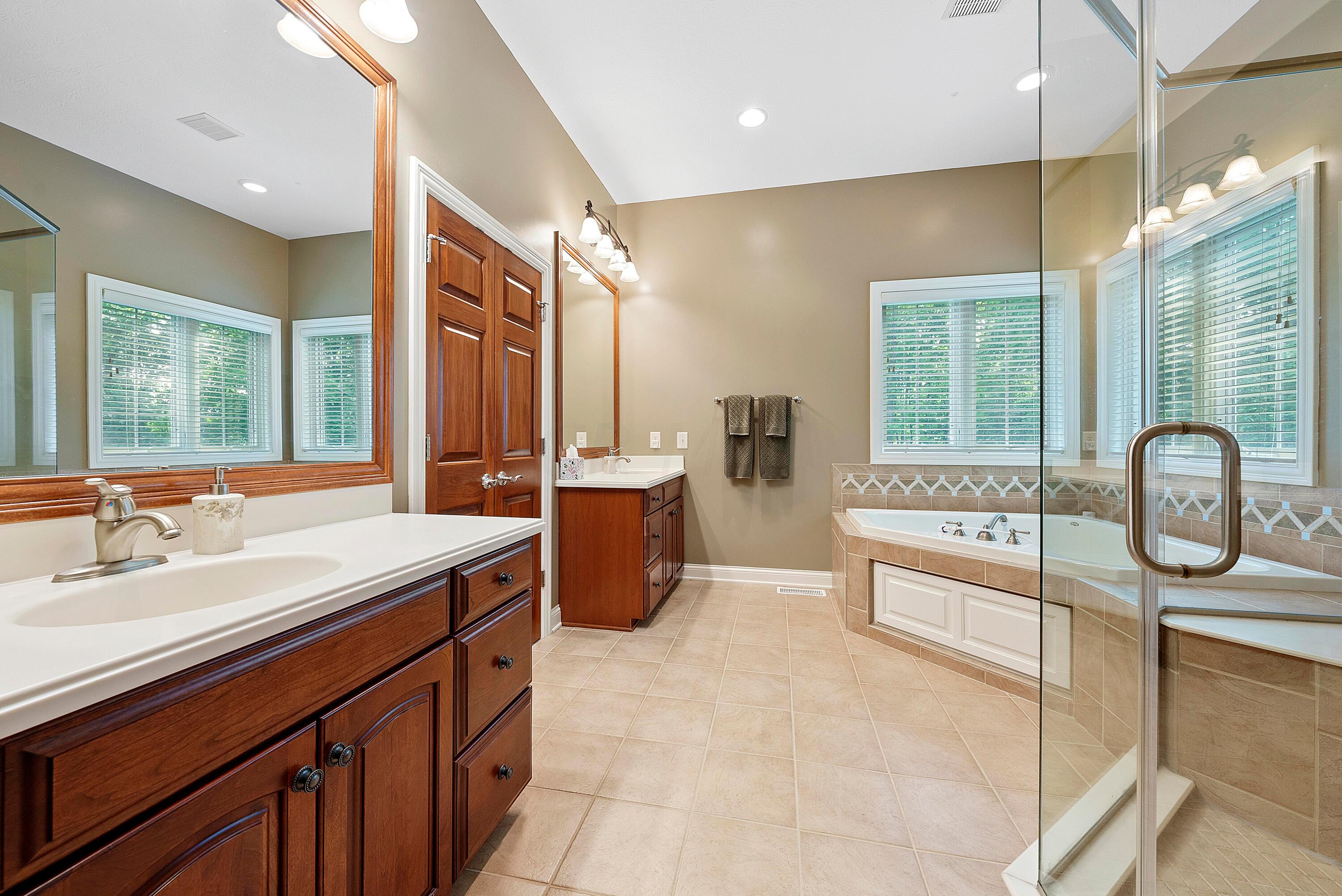 5761 Hughes Road Galena, OH 43021 - Photo 26 of 43 Luxurious ensuite Bathroom with a double door entry, ceramic tile flooring, 2 separate cherry vanities with sinks, mirrors and light bars, fabulous corner whirlpool tub with 2 windows above, a glass enclosed shower with custom tile surround and bench seat, 10’ ceiling, linen closet