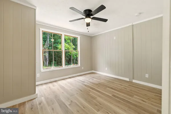 an empty room with wooden floor chandelier fan and windows