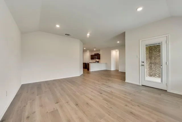 a view of empty room with wooden floor and kitchen