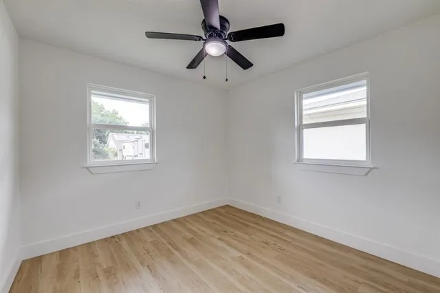 an empty room with wooden floor ceiling fan and windows