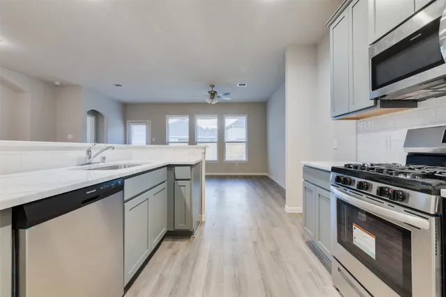 a kitchen with stainless steel appliances a sink dishwasher stove and microwave with wooden floor