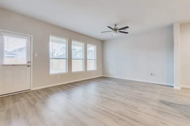 an empty room with wooden floor ceiling fan and windows