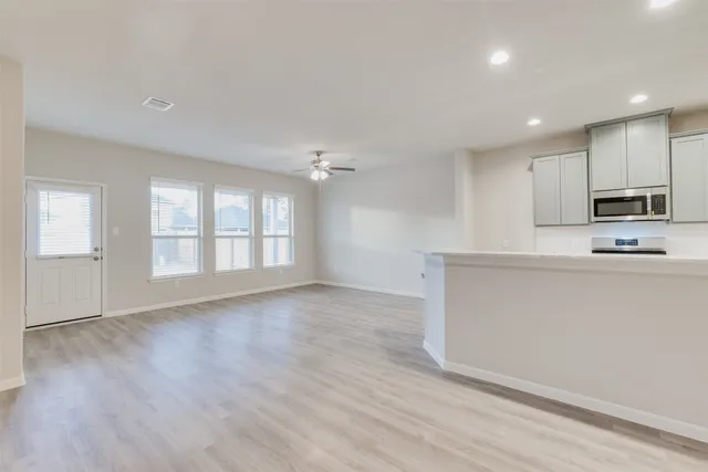 a view of an empty room with kitchen and window