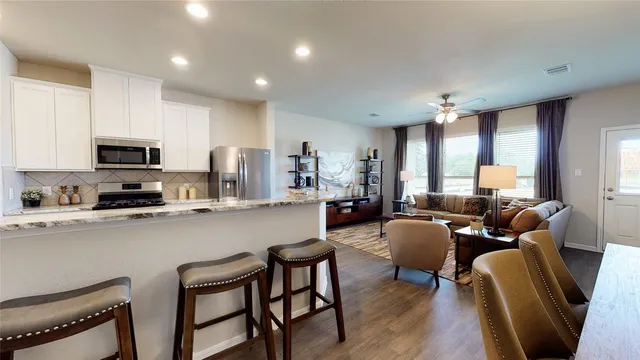 a living room with stainless steel appliances a dining table wooden floor windows and a kitchen view
