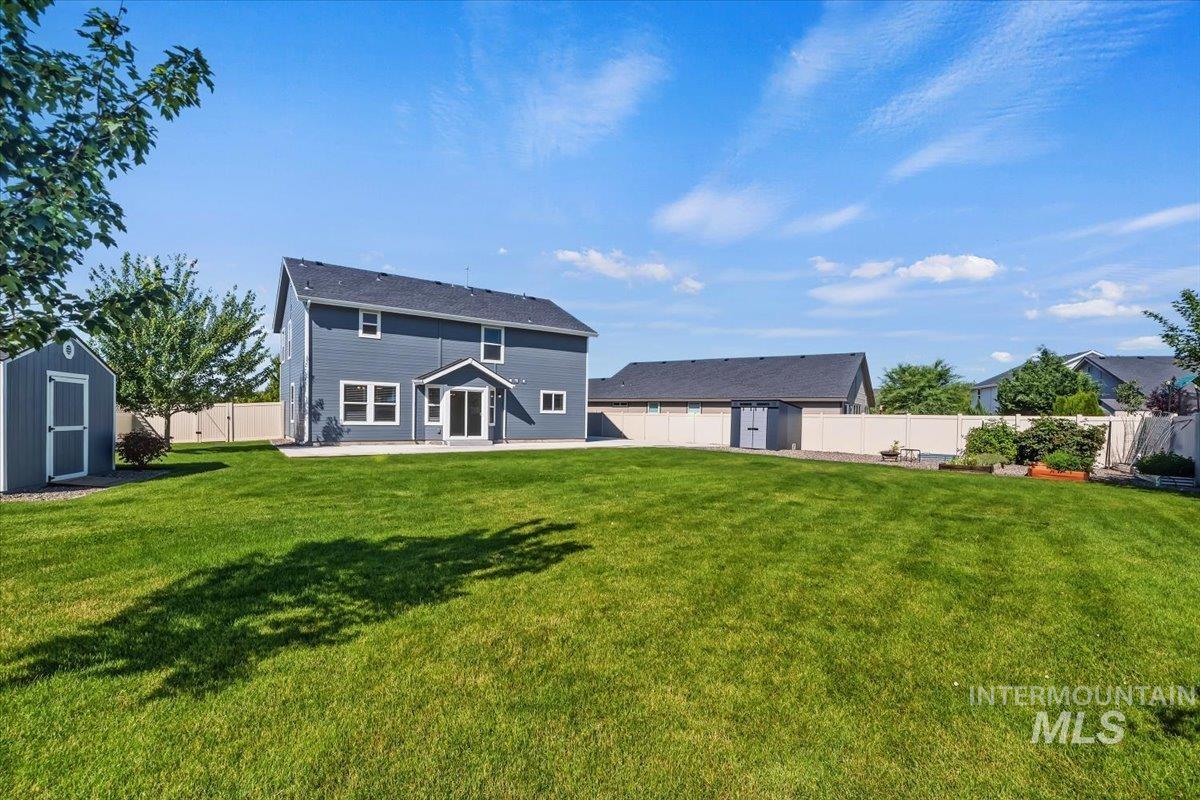 12310 West Hidden Point Drive Star, ID 83669 - Photo 2 of 48 Expansive backyard featuring a large green lawn, two-story residence with blue siding, white trim windows, and a patio area