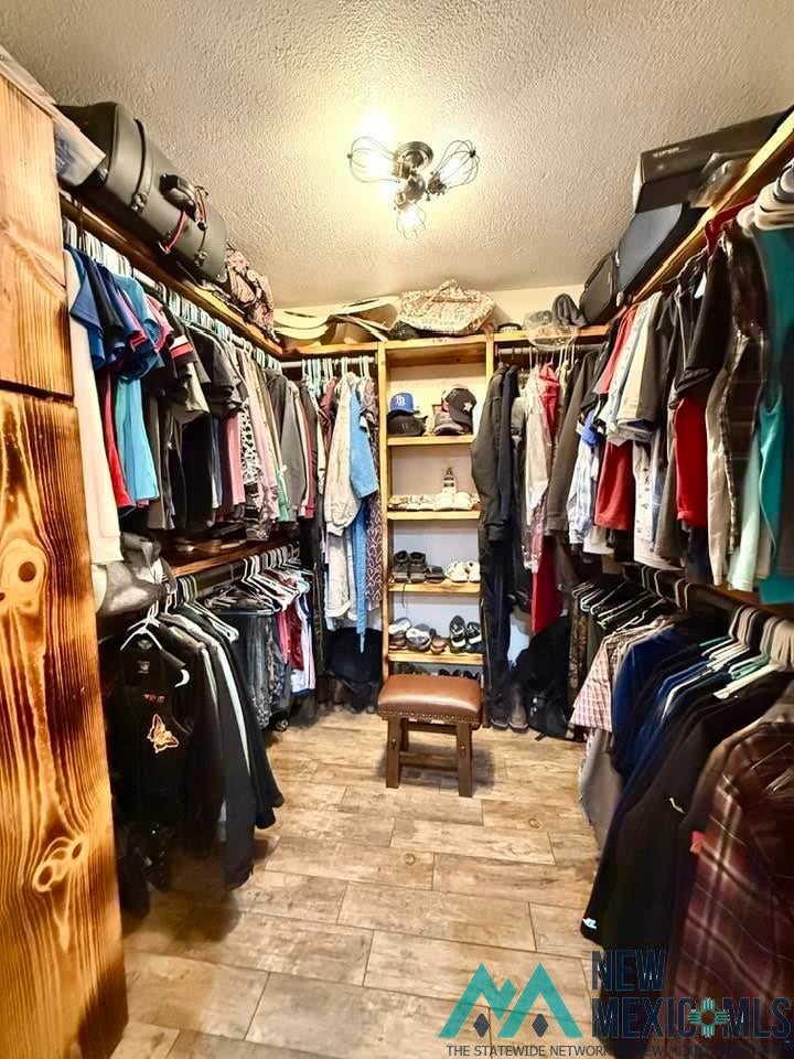 5404 Sioux Road Carlsbad, NM 88220 - Photo 55 of 100 Spacious walk-in closet featuring extensive built-in shelving, hanging rods, wood-finish flooring, a ceiling-mounted light fixture, and textured ceilings