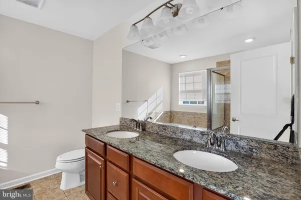 a bathroom with a granite countertop double vanity sink a mirror and a toilet