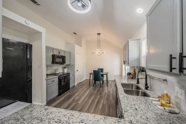 a kitchen with stainless steel appliances granite countertop a stove top oven a sink dishwasher a dining table and chairs with wooden floor